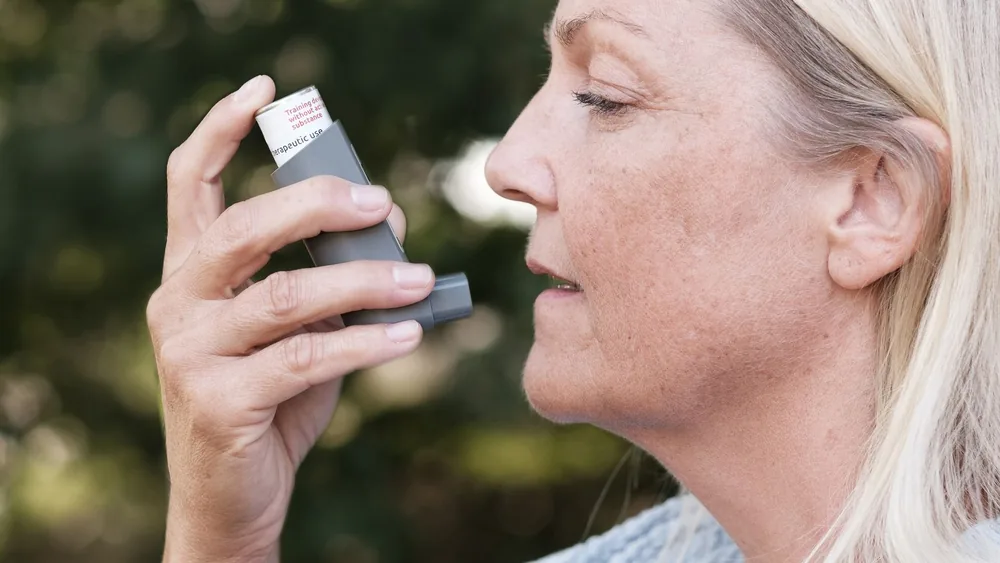 Woman using an inhaler outdoors to manage her respiratory condition effectively.
