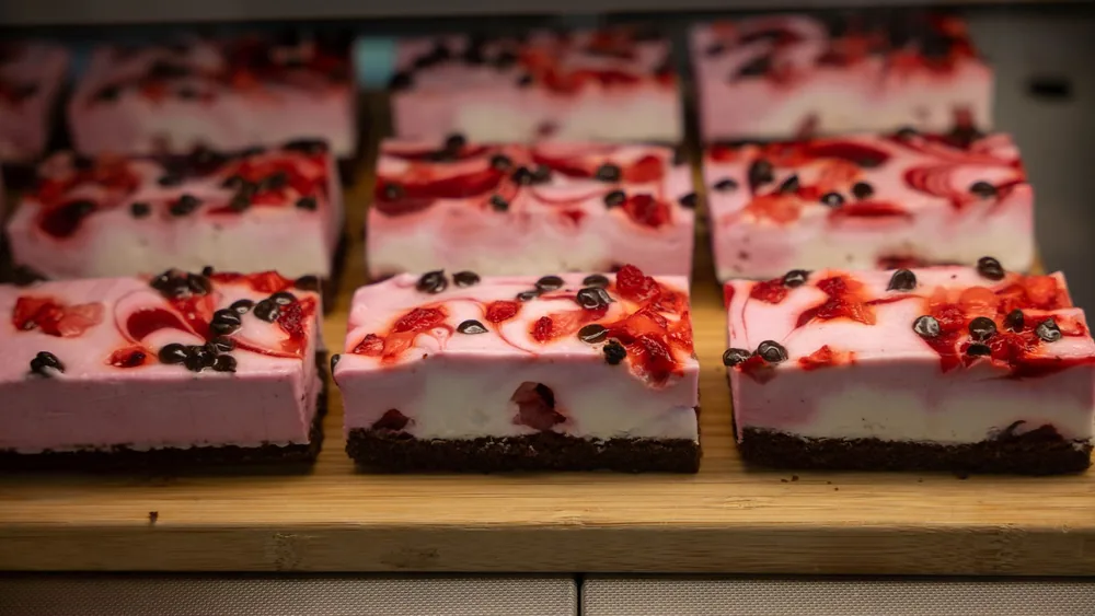 Sliced raspberry and chocolate layered cakes displayed on a wooden surface in a bakery, Zagreb.