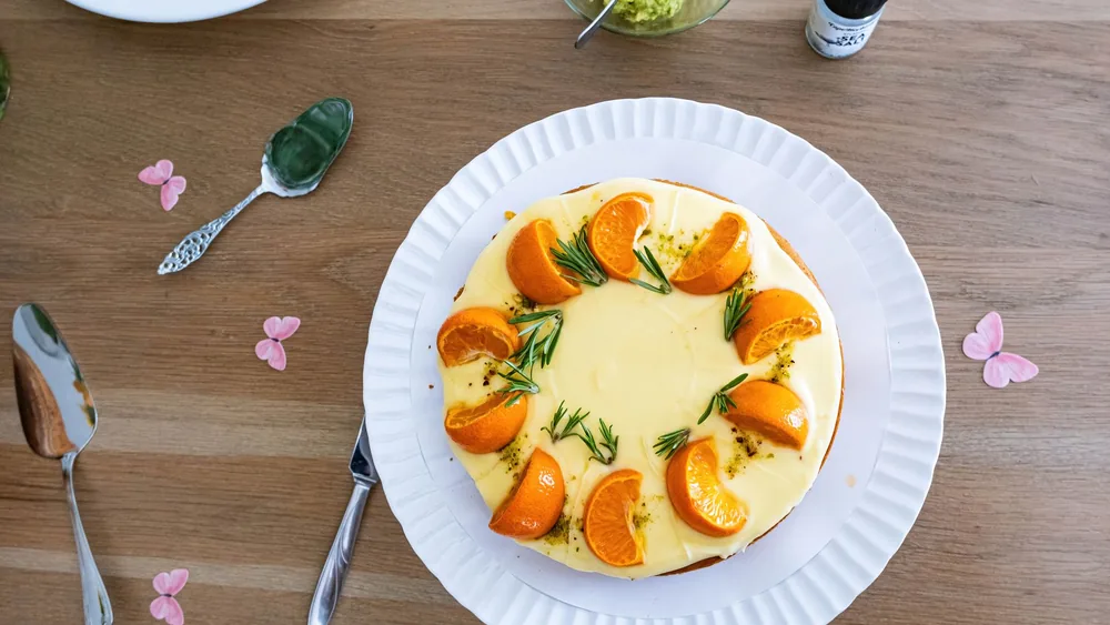 Delicious orange and rosemary cake presented on a wooden table with decorative flowers.