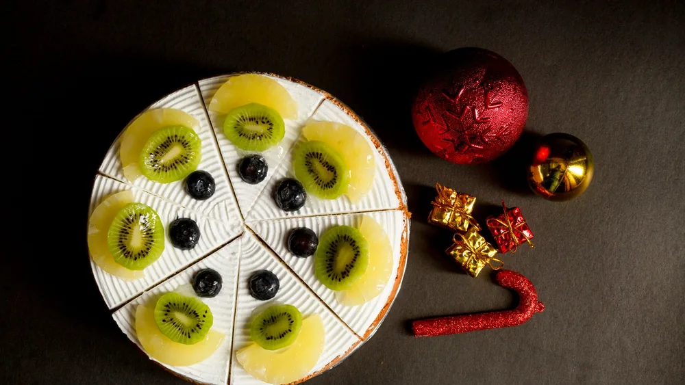 Sliced kiwi and berry dessert with Christmas ornaments on a dark background.