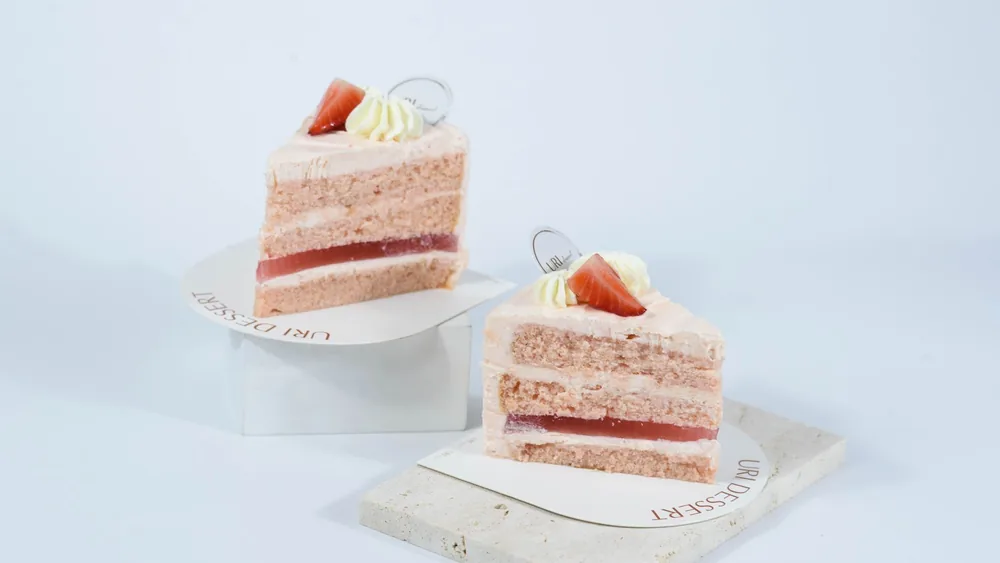 Close-up of two slices of pink layered cake with strawberry garnish on white background. Perfect for dessert themed presentations.