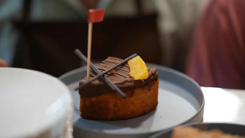 Close-up of a chocolate orange cake with flag decoration, served on a blue plate.