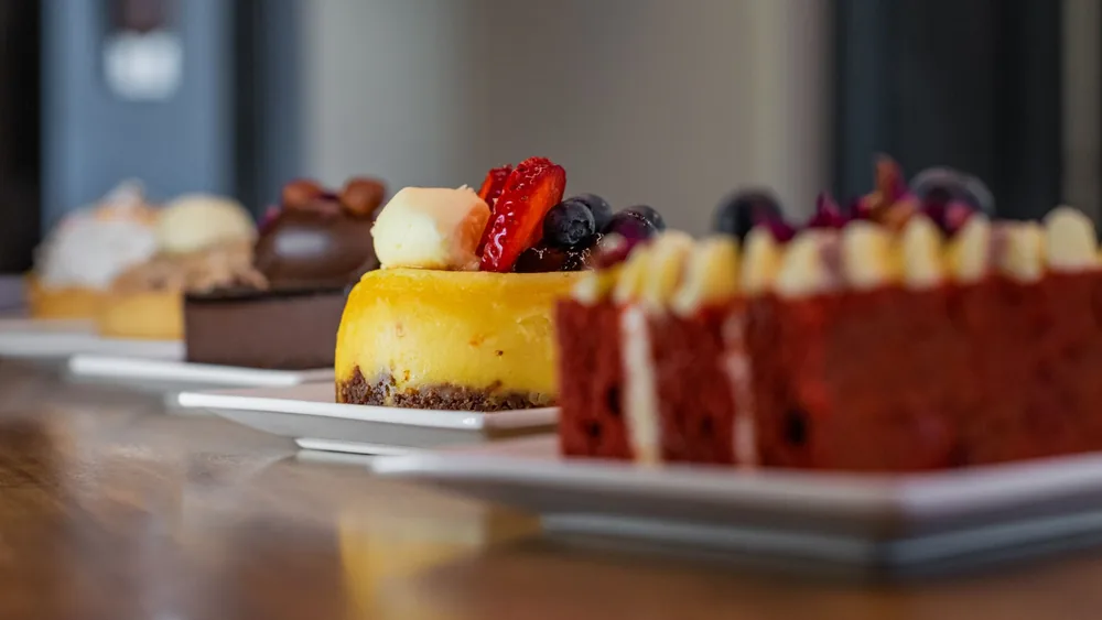 Close-up of assorted gourmet desserts on plates, featuring cheesecake, chocolate cake, and red velvet.