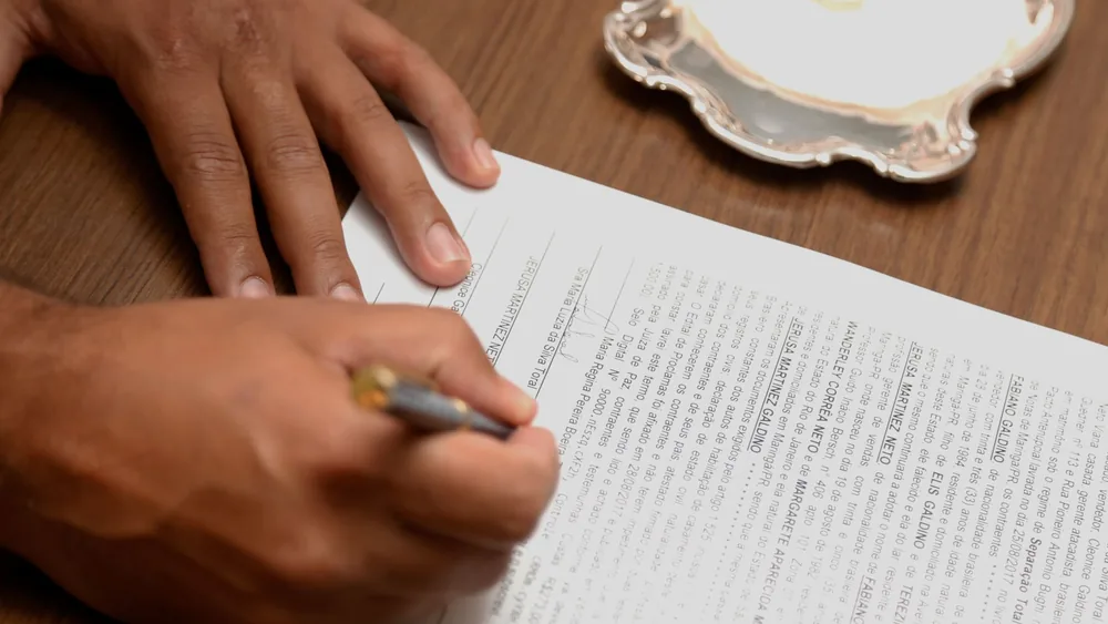 Hand signing a contract on a wooden desk, emphasizing business formalities.