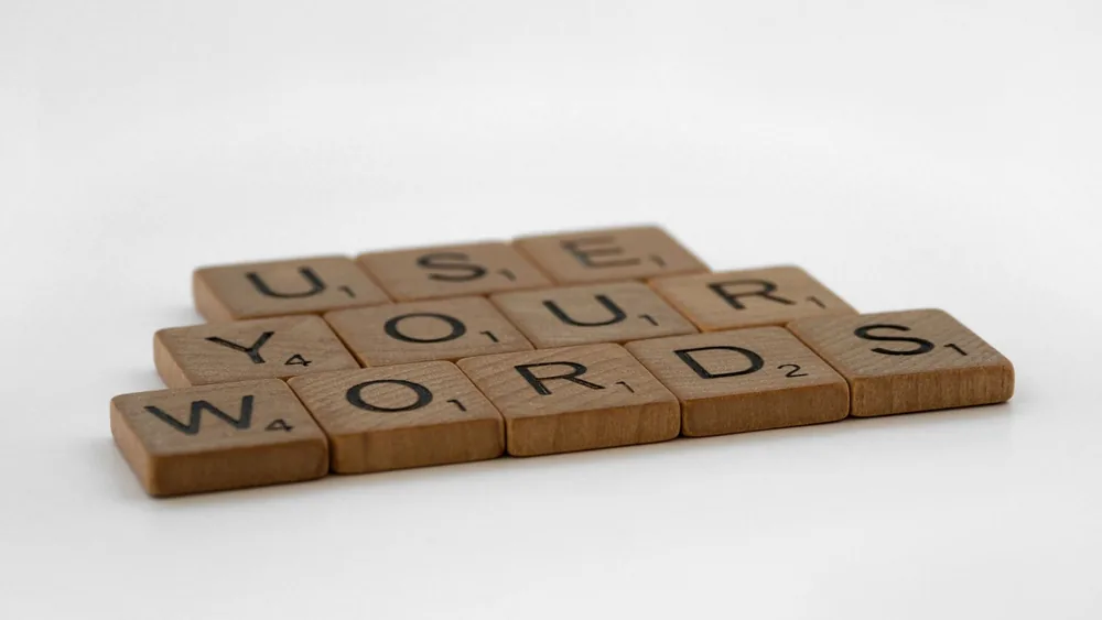 Close-up of wooden letter tiles spelling 'Use Your Words' on a white background, perfect for communication and language themes.