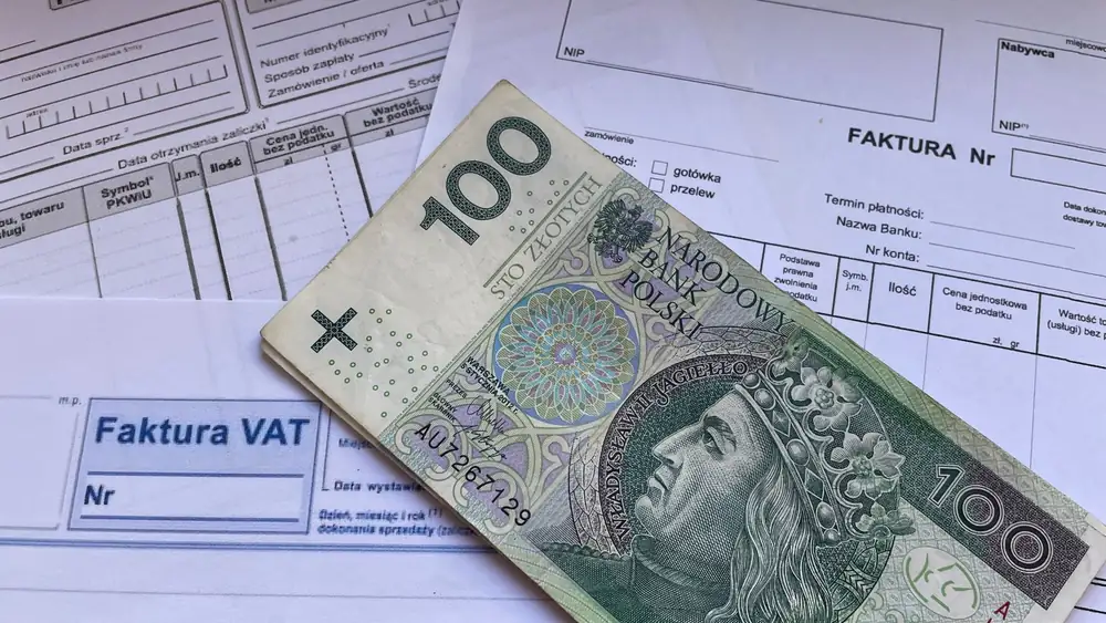 A 100 Polish Zloty note placed on top of business VAT invoices, symbolizing finance and economics.