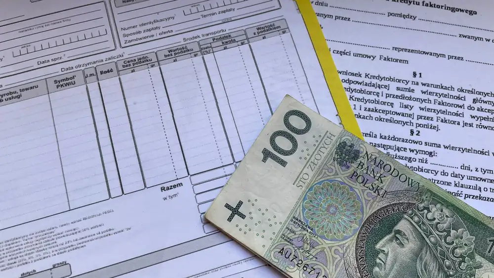100 Polish zloty bill on top of financial documents and invoices on desk.