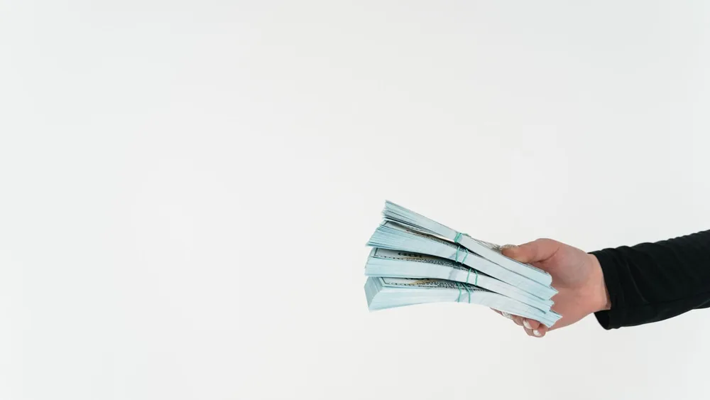 Close-up of a hand holding bundles of American dollar bills against a white background.