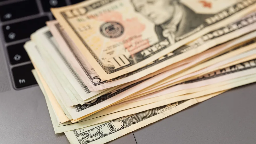Stack of US dollar bills on a keyboard, symbolizing digital finance and wealth.