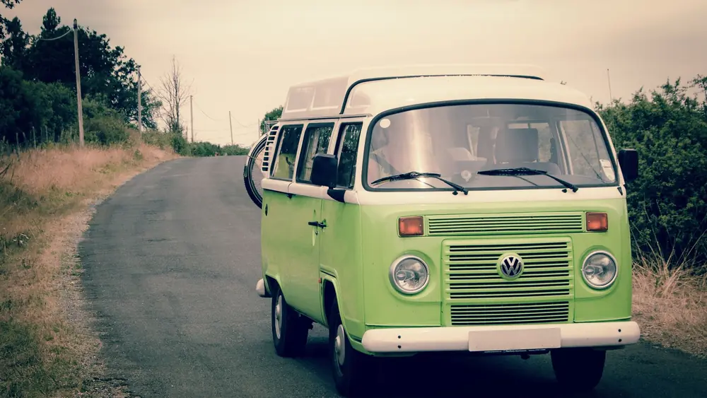 Classic green Volkswagen campervan driving on a quiet country road, perfect for road trips and adventure in nature.