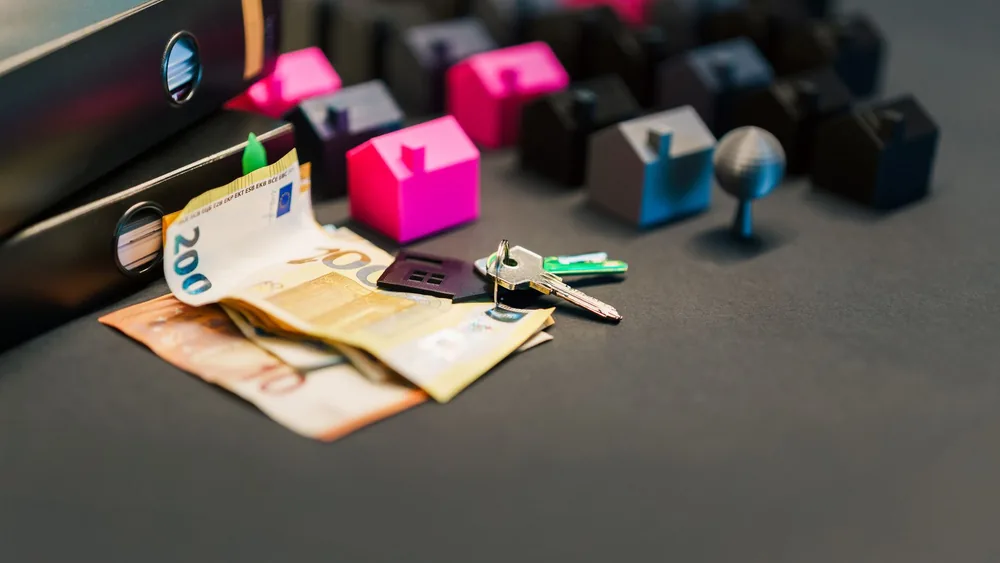 Miniature houses, euro bills, and a house key symbolize real estate investment and property transactions.