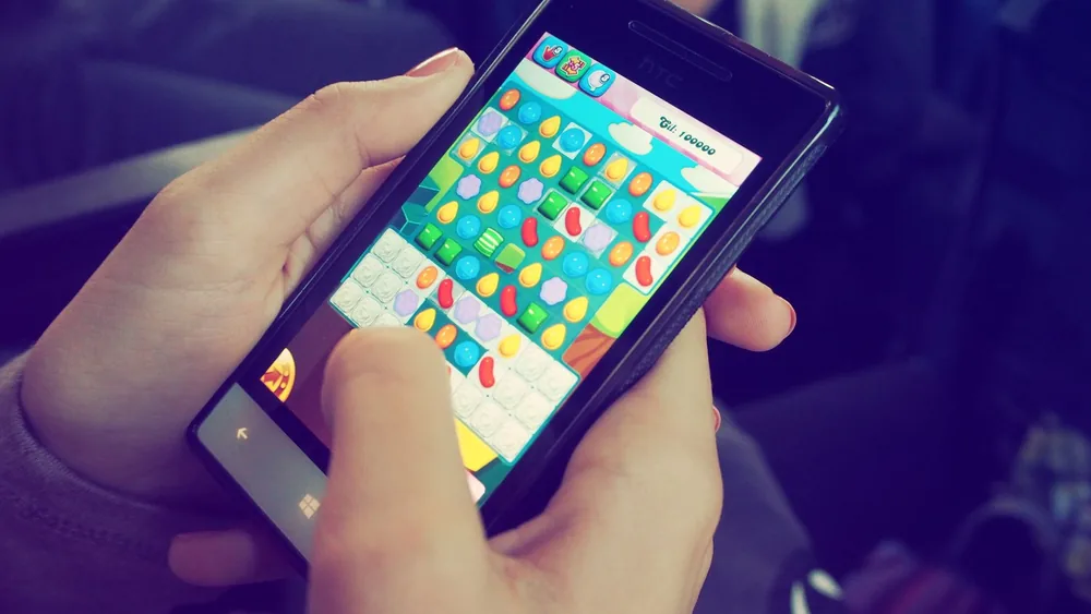 Hands holding a smartphone with a colorful puzzle game on the screen, displaying modern technology.