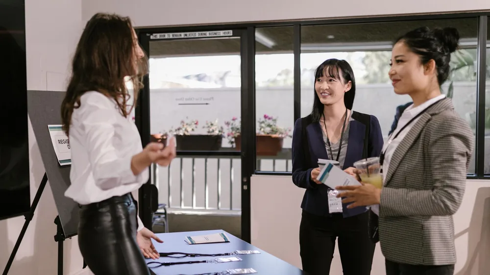 Businesswomen registering at a conference desk, smiling and interacting in a professional setting.