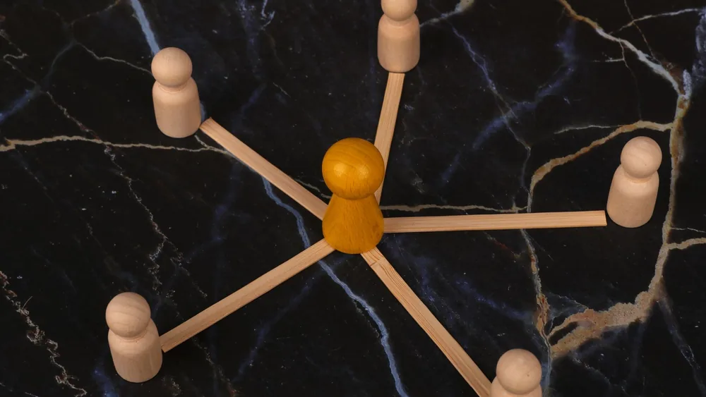 Wooden figures arranged in network pattern on dark marble background, symbolizing communication.